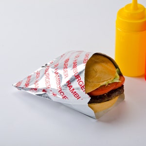 May include: A hamburger wrapped in a silver foil wrapper with the word "HAMBURGER" printed in red. The burger has a sesame seed bun, lettuce, and tomato. Yellow and red squeeze bottles are in the background.