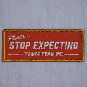 May include: Red embroidered patch with gold stitching. The patch says "Please... STOP EXPECTING THINGS FROM ME."