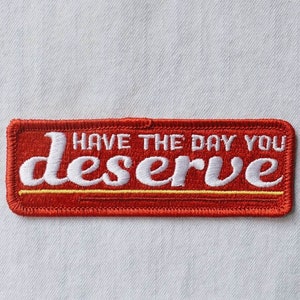 May include: Red embroidered patch with white stitching that reads "Have the day you deserve".