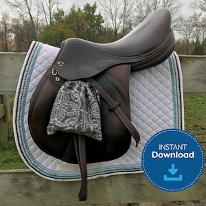 May include: A brown leather saddle with a white quilted saddle pad. The saddle is hanging on a wooden fence. The saddle has a small gray bag attached to it.