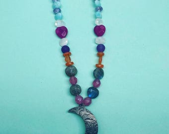 May include: A colorful beaded necklace with a crescent moon pendant. The necklace features blue, green, purple, orange, and pink beads.
