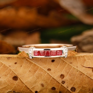 May include: A rose gold band ring with a row of five square-cut red rubies and small diamonds on either side.
