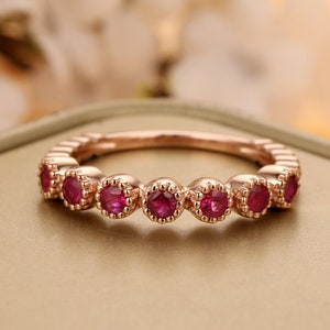 May include: A rose gold band ring with seven red ruby stones set in a scalloped design.