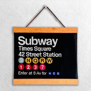 Puede incluir: Un letrero de metro negro y blanco con el texto "Subway Times Square 42 Street Station" y las líneas de metro "S N Q R W 1 2 3 7" y el texto "Enter at 8 Av for A C E".