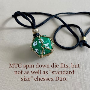 May include: A green twenty-sided die with white numbers is encased in a gold metal cage and hangs from a black leather cord. MTG spin down die fits, but not as well as "standard size" chessex D20.