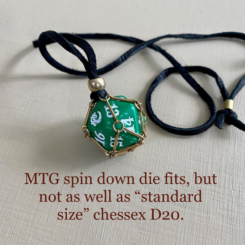 May include: A green twenty-sided die with white numbers is encased in a gold metal cage and hangs from a black leather cord. MTG spin down die fits, but not as well as "standard size" chessex D20.