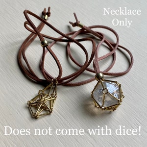 May include: Two brown leather cord necklaces with gold metal clasps. One necklace has a gold geometric pendant, the other has a gold cage with a clear glass twenty-sided die inside. "Necklace Only" and "Does not come with dice!" are written in black text on a white background.