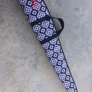 May include: A black and white patterned gun case with a black carrying handle. The case has a geometric design with a red monogram.