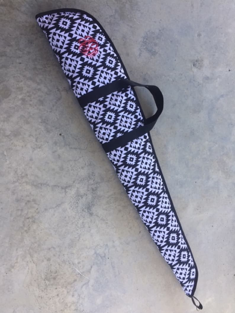 May include: A black and white patterned gun case with a black carrying handle. The case has a geometric design with a red monogram.