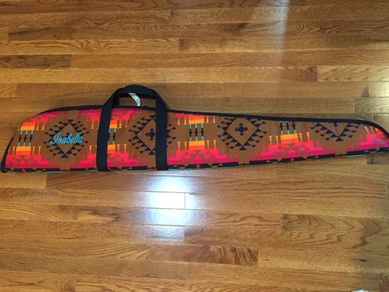 May include: A brown, black, red, orange, and turquoise patterned gun case with a black handle and the name "Isabella" embroidered on the front.