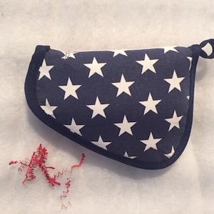 May include: A blue fabric pouch with white stars and a navy blue trim. The pouch has a loop handle and is lying on a white surface.