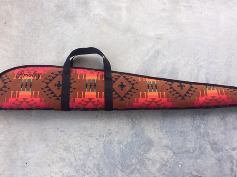 May include: A brown and red patterned gun case with a black handle and the name "Presley" embroidered on the front.