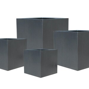 May include: A collection of four dark grey, cube-shaped planters in different sizes. The planters have a minimalist design and a matte finish. The open tops are visible, indicating they are intended for plants or decorative purposes. Measurements are in cm.