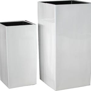 May include: Two white, square planters with a glossy finish. The planters have a black interior and a modern, minimalist design. One planter is taller than the other, offering a tiered look for displaying plants or decor.