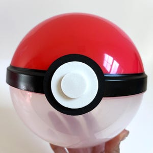 May include: A red and white Poke Ball with a black band around the middle. The Poke Ball is made of plastic and has a clear, translucent bottom.