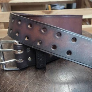 May include: A brown leather belt with a silver buckle. The belt has multiple rows of stitching and a distressed look.