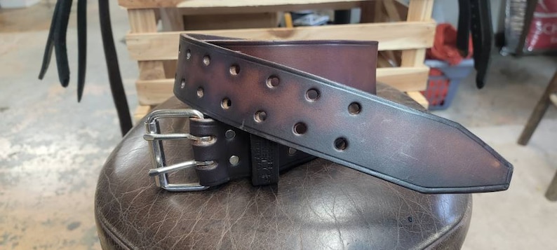 May include: A brown leather belt with a silver buckle. The belt has multiple rows of stitching and a distressed look.