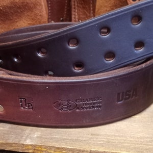 K&ouml;nnte beinhalten: Ein brauner Lederg&uuml;rtel mit einem schwarzen Lederg&uuml;rtel dar&uuml;ber. Der G&uuml;rtel hat eine Messingschnalle und der Text "Graber Harness & Saddlery USA" ist in das Leder gepr&auml;gt.