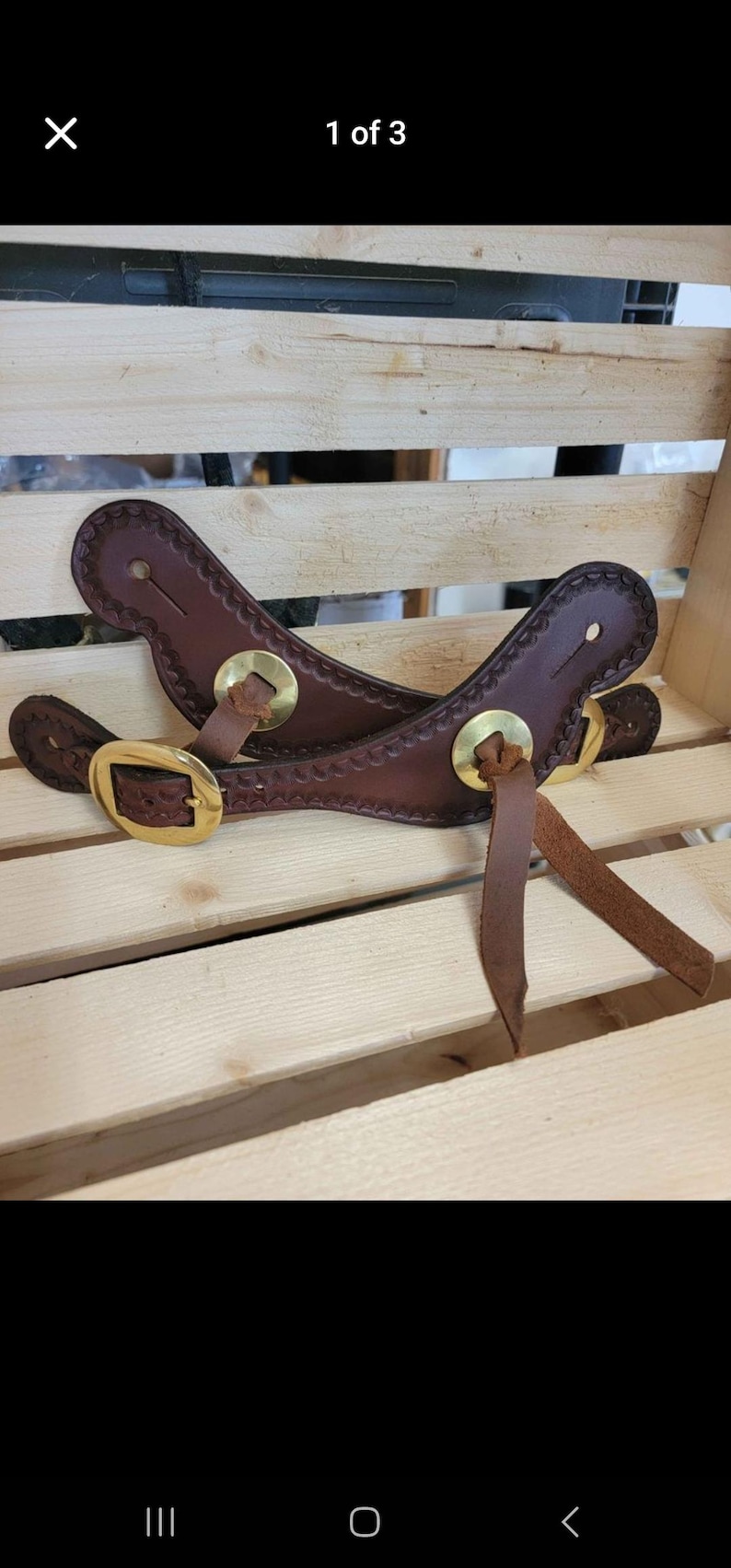Pu&ograve; includere: Due cinturini per speroni in pelle marrone con fibbie e punte in metallo dorato. I cinturini sono su una superficie di legno.