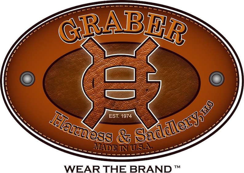 K&ouml;nnte beinhalten: Ein braunes, ovales Lederlogo mit dem Text "GRABER" in wei&szlig;er Serifenschrift. Das Logo enth&auml;lt auch ein stilisiertes "G" in der Mitte, mit dem Text "EST. 1974" darunter. Der Text "Harness & Saddlery, LLC" befindet sich unter dem "G" und der Text "MADE IN U.S.A." darunter. Der Text "WEAR THE BRAND TM" befindet sich unter dem Logo.