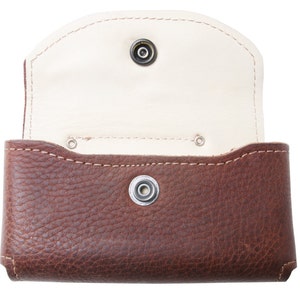 May include: A brown leather wallet with a white interior and a snap closure. The wallet is open and the interior is visible.