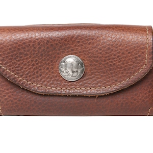 May include: A brown leather wallet with a flap closure and a silver coin-shaped button. The button features a buffalo design.