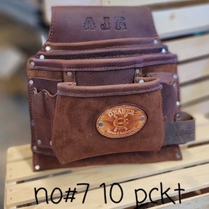 May include: A brown leather tool belt with multiple pockets and rivets. The belt has the initials "AJR" embossed on the top flap and a "GRABER" logo on the front pocket. The text "no#7 10 pckt" is written at the bottom.