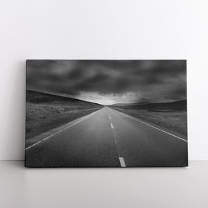 May include: A black and white photograph of a long, straight road disappearing into the distance under a cloudy sky.