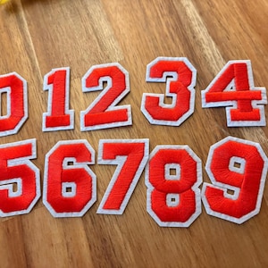 May include: Red felt numbers with white outlines, from 0 to 9, on a wooden surface.