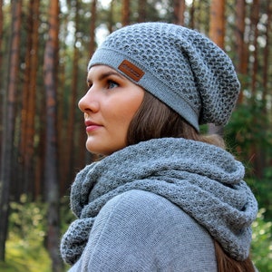 May include: A woman wearing a gray knitted beanie and matching scarf. The beanie has a small brown leather tag with the word "Nordic" on it.