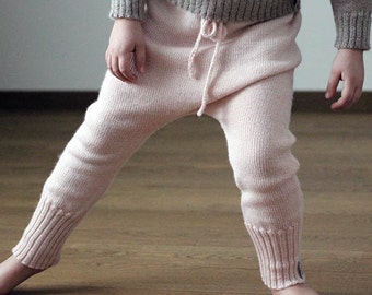 May include: A child wearing a light gray sweater and pink knit pants with a drawstring waist.