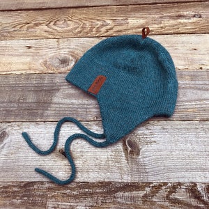 Peut inclure: Chapeau en tricot bleu sarcelle avec une sangle en cuir et une longue cravate. Le chapeau est sur un fond en bois.