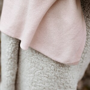 May include: A soft, pink blanket with a fuzzy, white texture. The blanket is folded in half and the pink side is facing the camera.