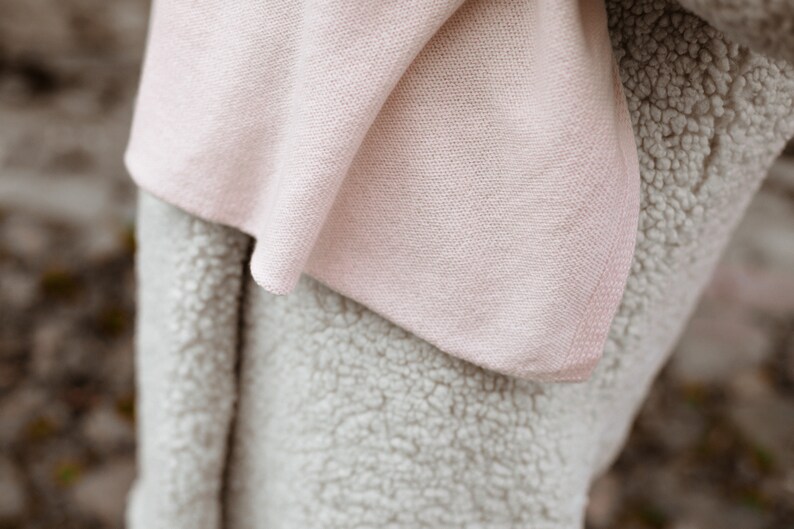 May include: A soft, pink blanket with a fuzzy, white texture. The blanket is folded in half and the pink side is facing the camera.