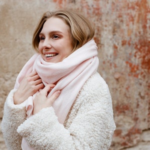 May include: A woman wearing a white fuzzy jacket with a pink scarf wrapped around her neck. She is smiling and looking to the right.