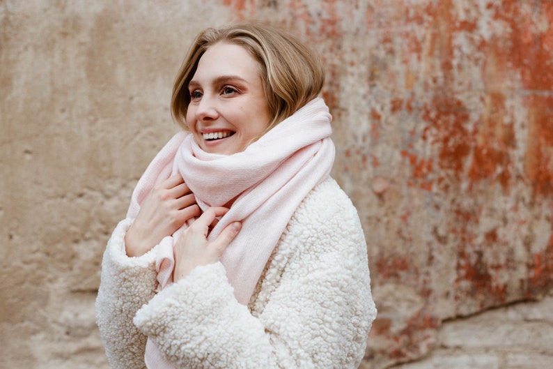 May include: A woman wearing a white fuzzy jacket with a pink scarf wrapped around her neck. She is smiling and looking to the right.