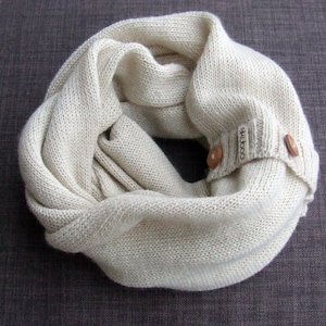 May include: A cream-colored knitted infinity scarf with two wooden buttons and a "coco" label.