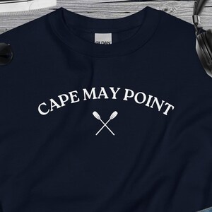 May include: A navy blue sweatshirt with the text "CAPE MAY POINT" in white, with two crossed oars underneath the text.