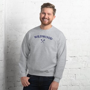May include: A gray sweatshirt with the word "WILDWOOD" in navy blue arched across the chest, with crossed oars beneath. The sweatshirt is a crew neck style and is made of a soft material.