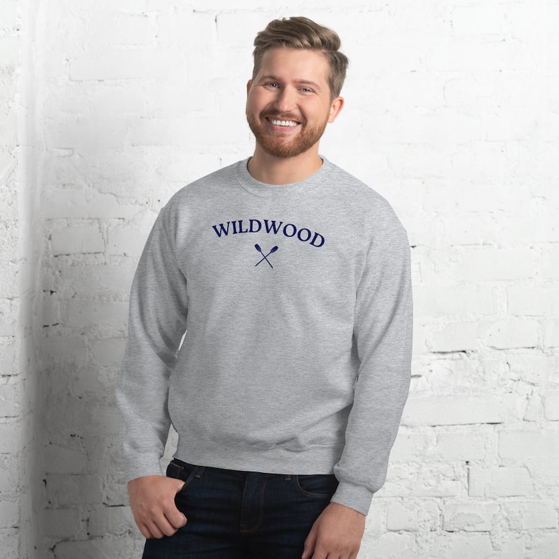 May include: A gray sweatshirt with the word "WILDWOOD" in navy blue arched across the chest, with crossed oars beneath. The sweatshirt is a crew neck style and is made of a soft material.