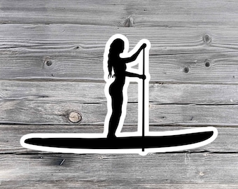 May include: Silhouette of a person standing on a paddleboard holding a paddle. The image is set against a wood grain background.