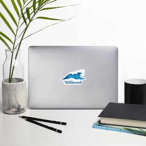 May include: A blue and white wave sticker with the text "Wildwood" on a silver laptop.