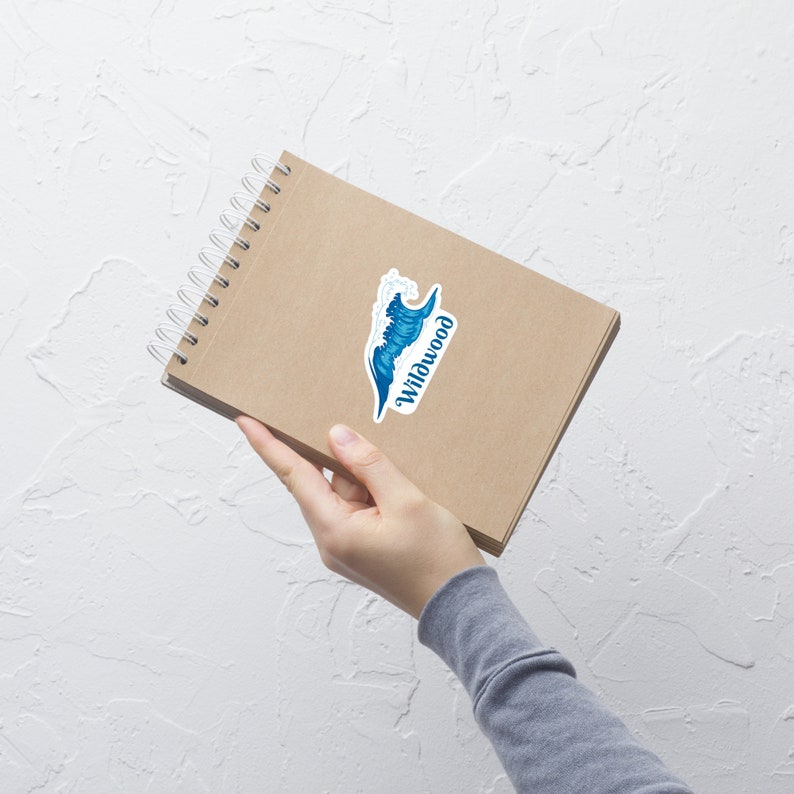 May include: A brown notebook with a spiral binding and a sticker of a blue wave with the word "Wildwood" on it.