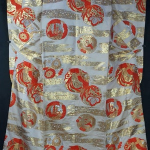 May include: A white silk kimono with a red and gold pattern of phoenixes and flowers. The kimono is decorated with gold thread and has a red trim.