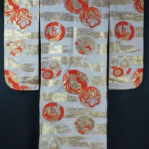 May include: A white kimono with a red and gold pattern of stylized birds and flowers. The kimono has a red trim around the edges.