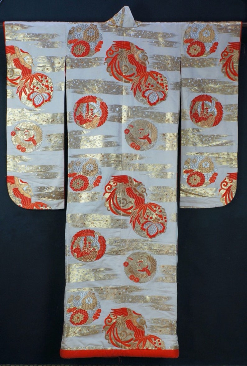 May include: A white kimono with a red and gold pattern of stylized birds and flowers. The kimono has a red trim around the edges.