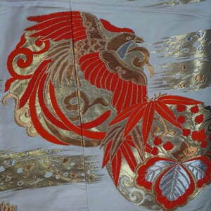 May include: A white fabric with a red and gold embroidered phoenix design. The phoenix is surrounded by red and gold leaves and flowers.