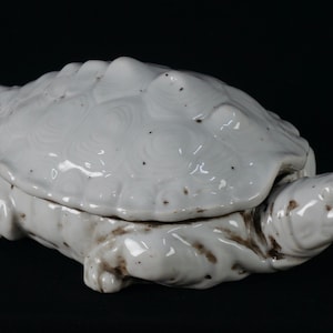 May include: White ceramic turtle-shaped dish with a lid. The turtle has a detailed shell and a realistic head.