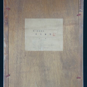 Puede incluir: Un marco de madera con una etiqueta de papel blanco en el interior. La etiqueta tiene texto japon&eacute;s que dice "第ニ記念会日" y "并 1: 安 功".