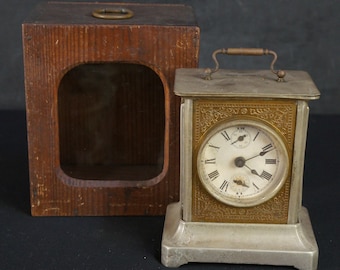 Puede incluir: Reloj despertador antiguo de plata y oro con una esfera blanca y agujas negras. El reloj está en una caja de madera con un frente de vidrio.